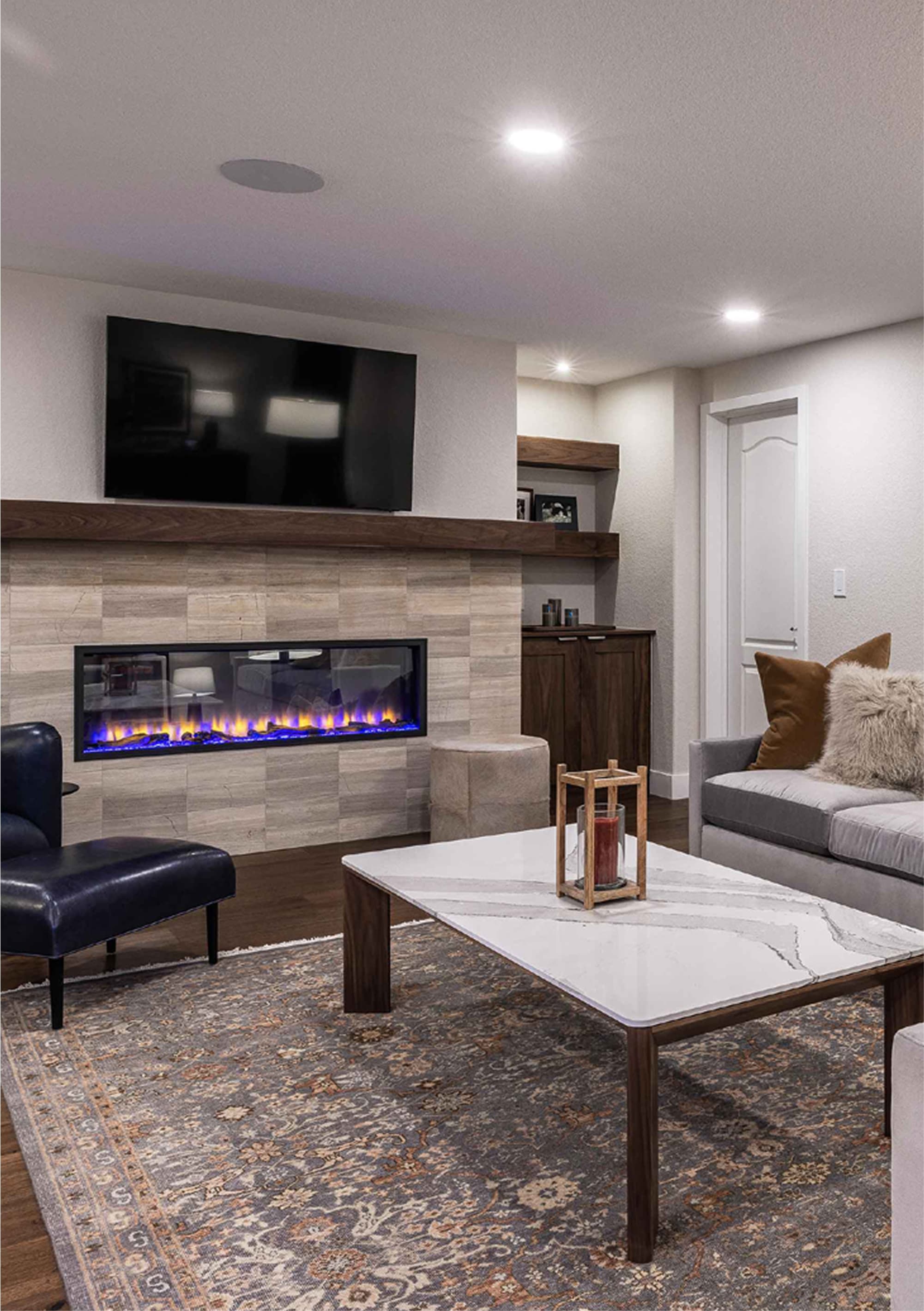 A modern living room featuring two sofas with decorative pillows, a coffee table, a lamp, and a wall-mounted TV. A fireplace with a stone surround adds warmth to the space, complemented by a decorative rug.