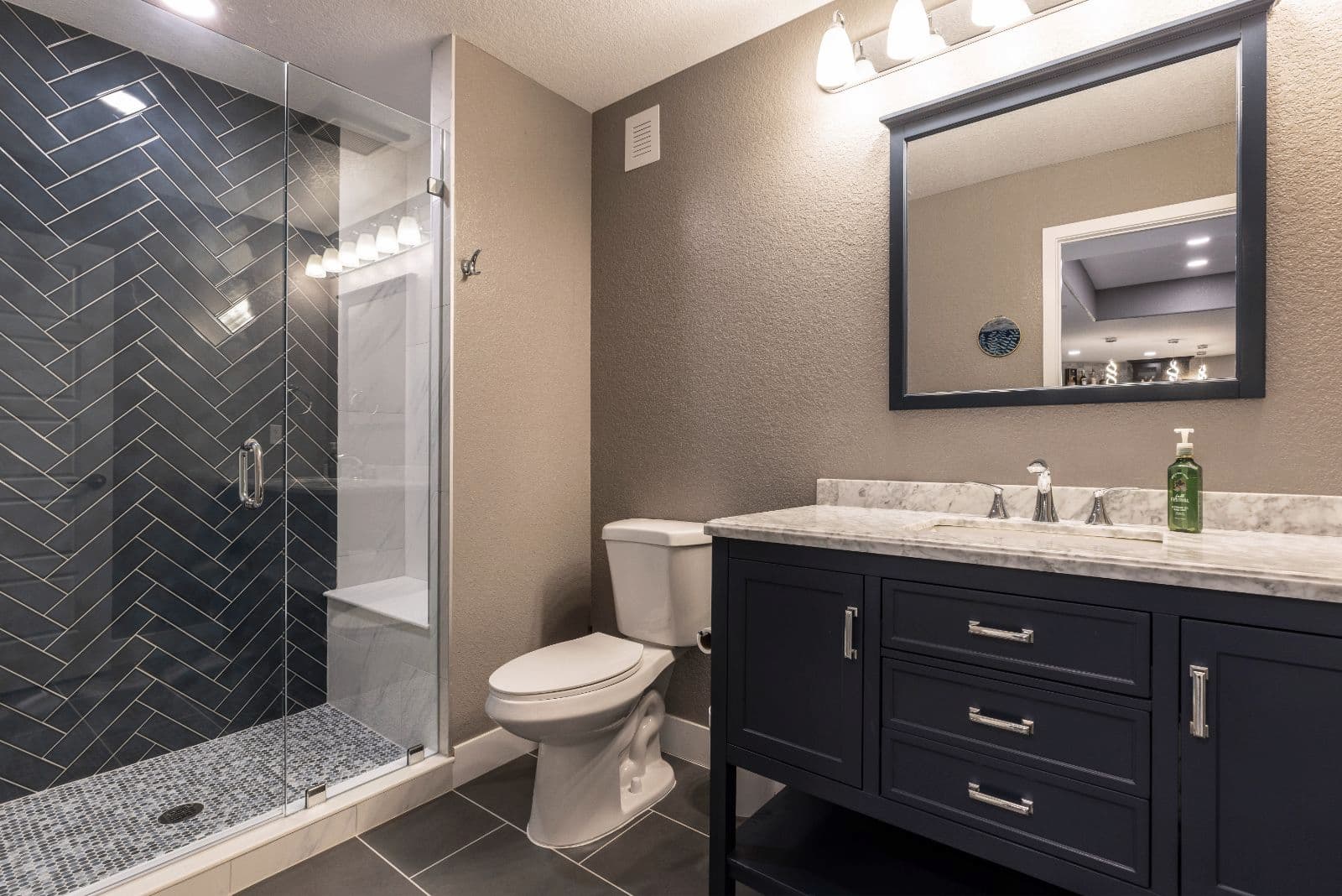 A modern bathroom featuring a glass shower, a navy blue vanity with a marble countertop, a toilet, and a mirror above the sink.