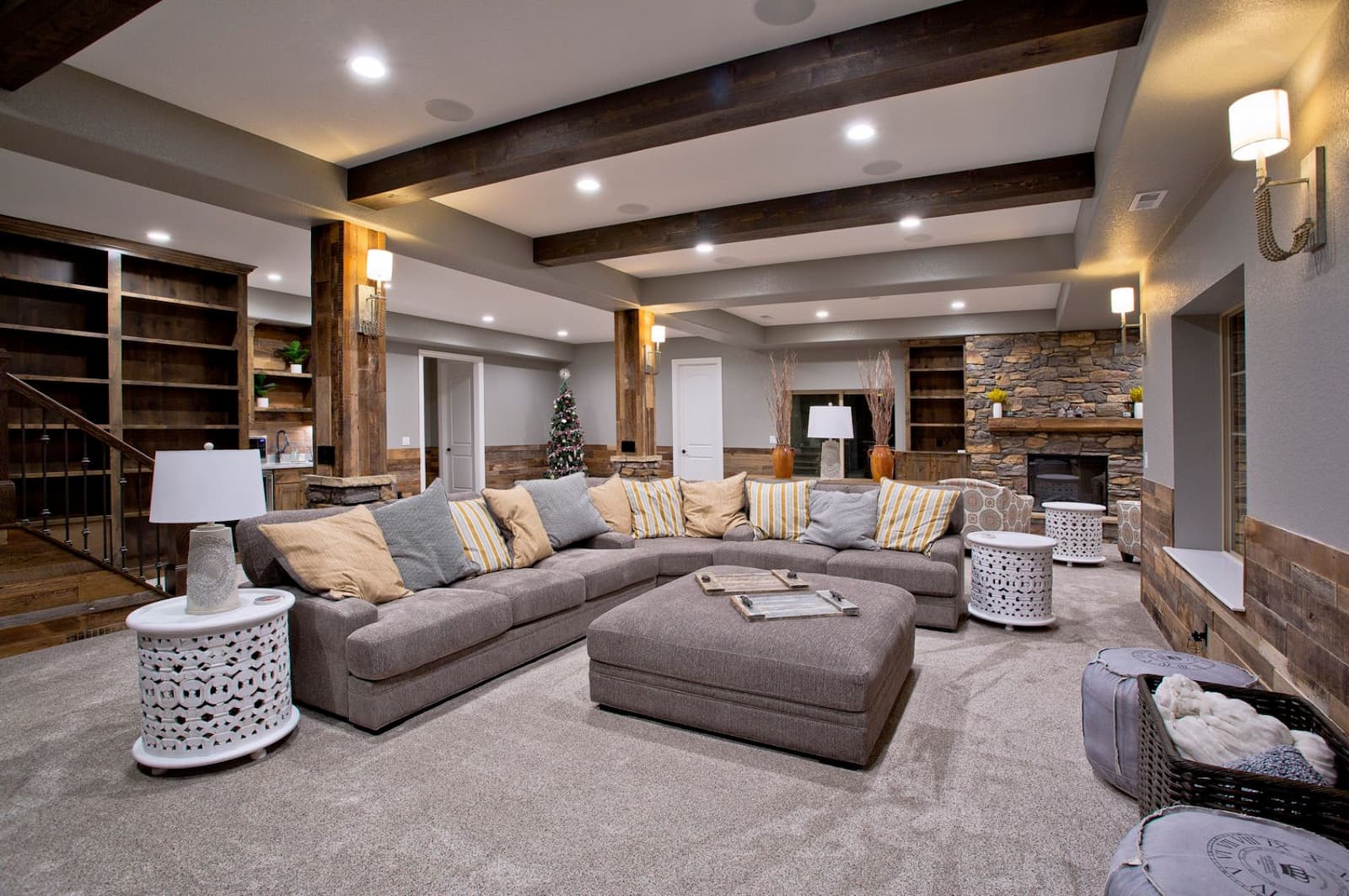 Cozy living room with a large sectional sofa, decorative pillows, a coffee table, and a Christmas tree. Wooden beams and stone accents add warmth to the space.