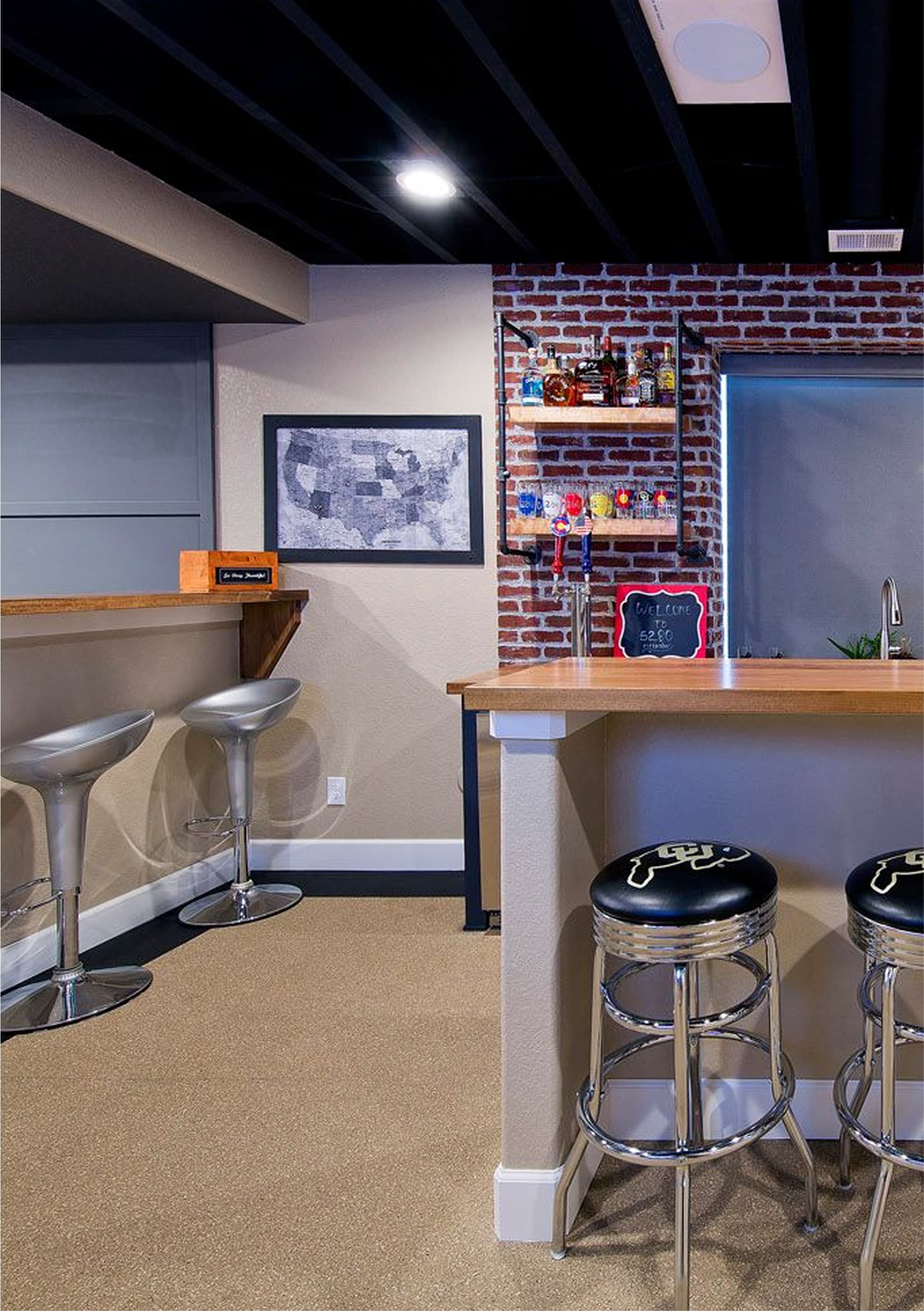 A modern home bar with a wooden counter, four chrome bar stools, a red refrigerator, and brick accent walls.