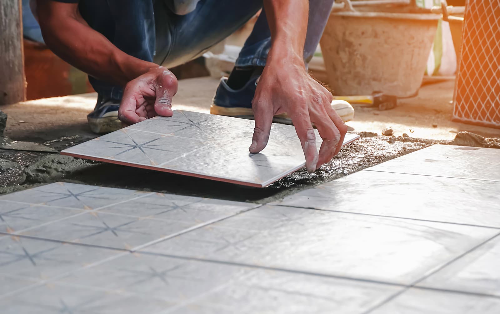 A person is laying a tile on a cemented floor, preparing it for installation.