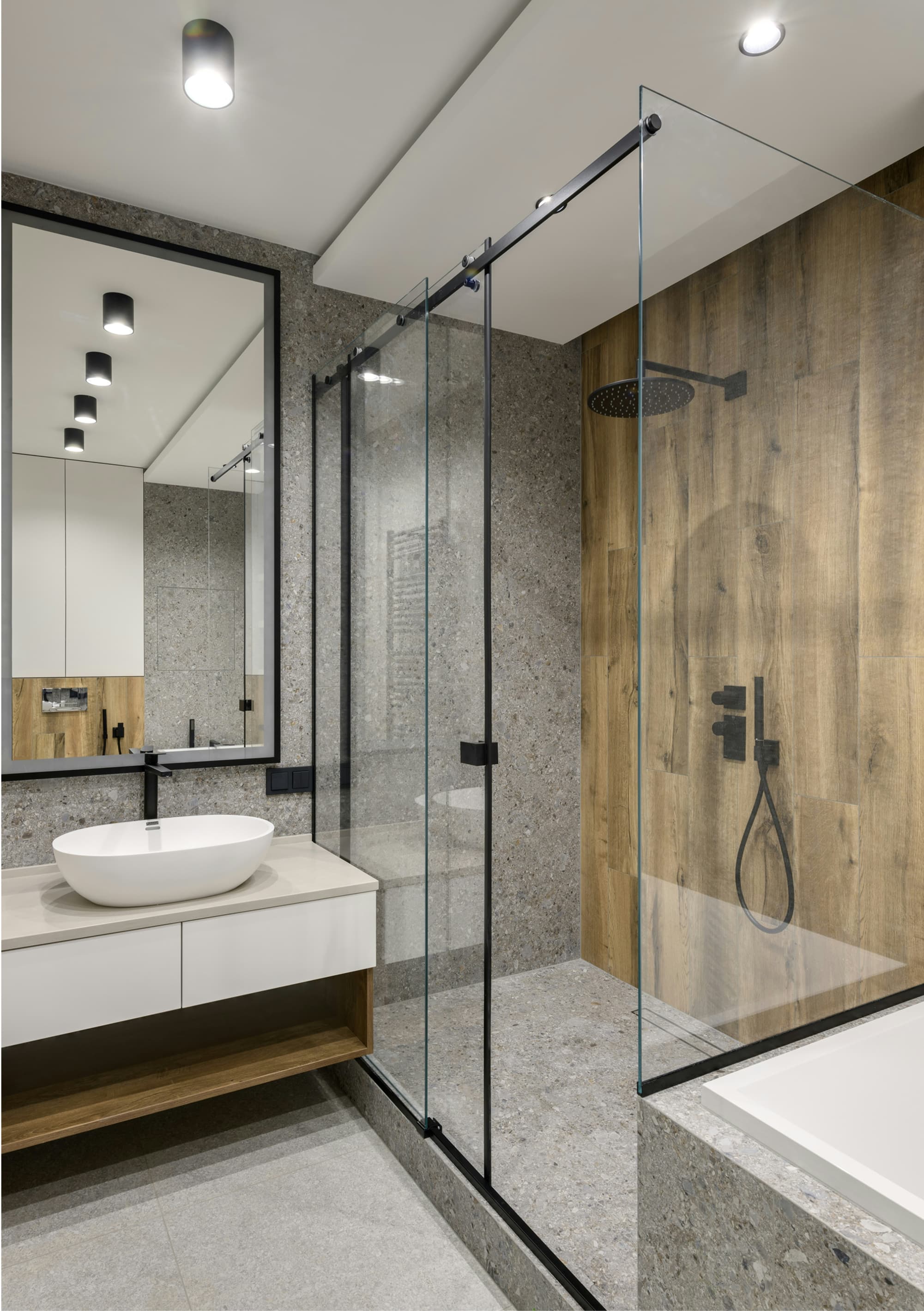 A modern bathroom featuring a glass shower, a wall-mounted sink with a sleek vanity, a mirror, and a bathtub with a minimalist design. The color scheme includes natural wood and stone elements.